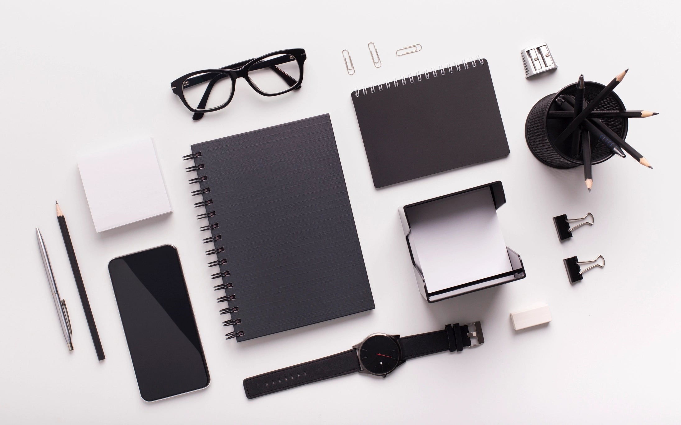 Collection of black office supplies including notebooks, phone, watch, and stationery on a white background
