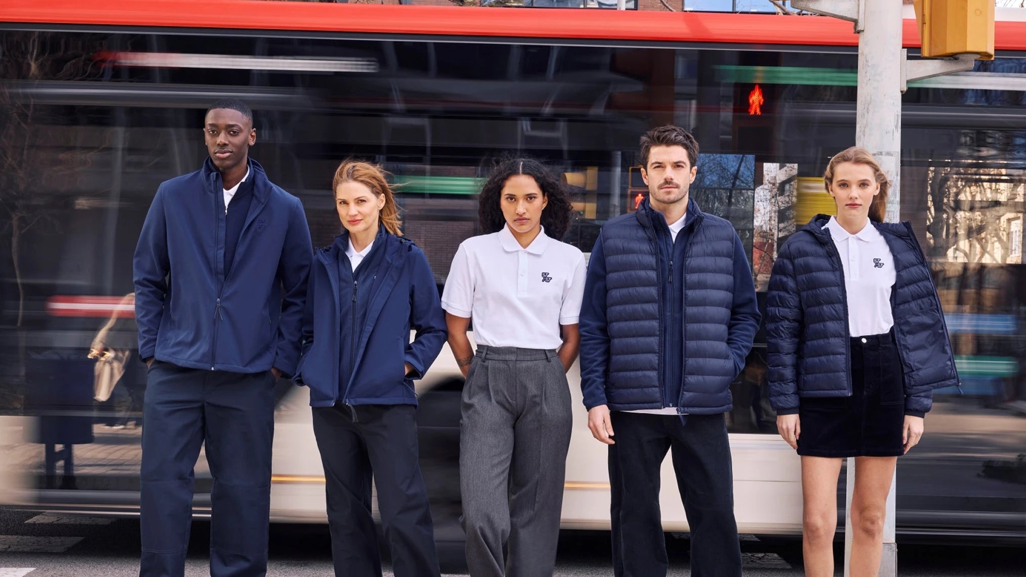 Five people in matching embroidered workwear standing in front of a bus.