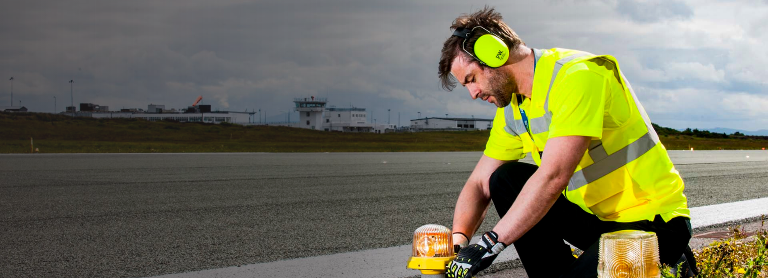 An adult in customised Portwest Hi-Vis workwear squats next to a road